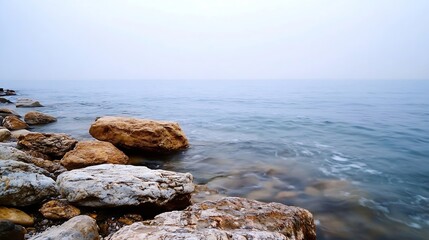 Aufkleber - Serene rocky shoreline with gentle waves and calm water on a foggy day creating a peaceful atmosphere : Generative AI