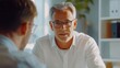 © GenFrameLab - A serious mature businessman in glasses attentively listens to his younger colleague du a private meeting in a modern office.