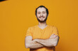 © SHOTPRIME STUDIO - Cheerful young man with a beard in an orange t shirt smiling against a vibrant yellow background, showcasing confidence and positivity