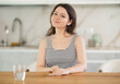 © JackF - Young smiling woman posing sitting at table in kitchen at home