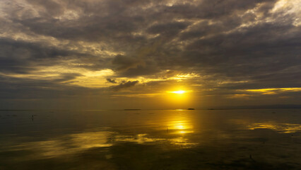 Wall Mural - sunset over calm waters with reflections and dramatic clouds