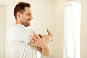 Aufkleber - Cheerful Guy Exercising Stretching Arms Training Standing At Home. Morning Physical Exercises, Male Fitness, Daily Workout Routine Concept. Copy Space For Text