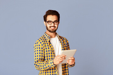 Poster - Online work, education or communication. Funky Indian man using tablet computer on violet studio background