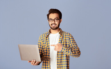 Poster - Online work, education, communication concept. Happy Indian guy pointing at laptop over lilac background