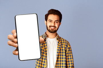 Poster - Smiling Indian guy showing smartphone with mockup for mobile app design on screen, violet background