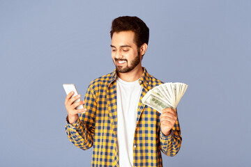 Poster - Millennial Indian guy with cash making money online on mobile phone, lilac background