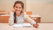 © Malik Nalik - A happy kid girl sitting at a school desk in the classroom, looking at the camera and smiling.