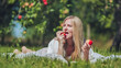 © Довидович Михаил - Young blond woman resting on blanket amid orchard trees, biting ripe red apple while sunlight streams across verdant landscape