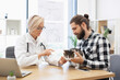 © sofiko14 - Male owner and female veterinarian discuss care of injured cat in clinic room. Veterinarian treats cat's injury, showing care and expertise, while owner shows concern and care for pet's wellbeing.