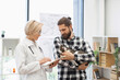 © sofiko14 - Female veterinarian discussing treatment plan with adult bearded man holding cat in clinic. Medical professional explaining pet care using tablet demonstrating attentive and professional consultation
