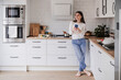 © Westend61 - Smiling woman in a modern kitchen using a mobile phone