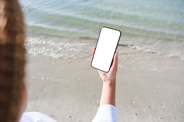 Wall Mural - mockup image of a woman holding mobile phone with blank desktop screen by the sea