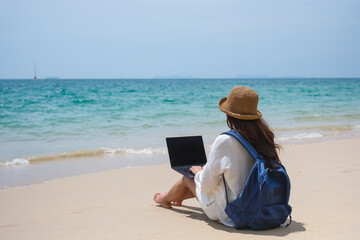 Wall Mural - a female traveler using and working on laptop computer while sitting on the beach