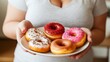 © iuricazac - A woman holding a plate of three donuts, each with different toppings, including sprinkles and chocolate.