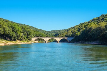 Poster - River flows under a historic stone bridge amidst lush greenery on a clear sunny day