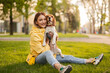 © kegfire - Cheerful woman enjoying time with her dog outdoors in a green park during a sunny day.