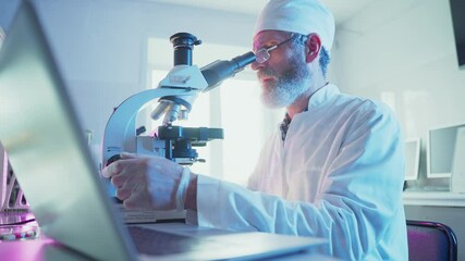 Wall Mural - laboratory technician in white coat using microscope and typing on laptop, performing scientific res