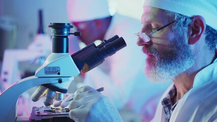 Wall Mural - bearded scientist wearing lab coat and surgical cap using microscope in a laboratory, checking sampl
