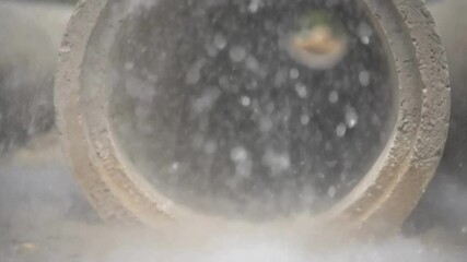 Poster - A closeup of a concrete pipe being vibrated to eliminate air bubbles with droplets of concrete splashing against the molds interior.