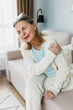 © shurkin_son - Vertical indoor image of senior lady in casual clothes suffering terrible unbearable pain in upper joints, holding her shoulder, having chronic bone disease, like arthritis or rheumatism