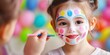 © Innavector - A young girl with colorful face paint happily brushes her teeth, showcasing a playful blend of fun and personal care in her daily routine.
