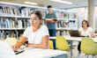 © JackF - Portrait of positive woman with laptop and book in public library