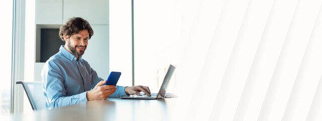 Poster - Cheerful mature businessman checking smartphone, using laptop computer, working online at company office, blank space. Professional occupation, business lifestyle concept