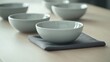 © Designs to Display - A modern table layout featuring pale gray dishes, a charcoal napkin, and a plain wooden table surface