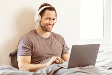 Aufkleber - Watch Movie Online. Man Using Laptop Wearing Headphones Watching Film Sitting In Bed In Bedroom At Home. Weekend Leisure, Educational Internet Website Advertisement And Freelance Lifestyle