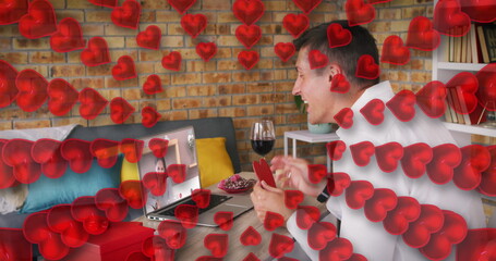 Poster - Heart icons against caucasian man holding a heart shaped placard while having a image call on laptop