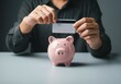© SERHII - Person holding credit card above pink piggy bank on gray table