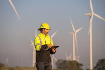 Fototapete - Engineer man working with tablet at windmill farm Generating electricity clean energy. Wind turbine farm generator by alternative green energy.