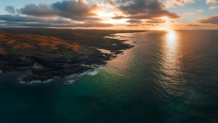 Wall Mural - Sunset Coast: Aerial View of Rugged Coastline, Setting Sun's Vibrant Hues Reflected on Water, Golden Light on Land, Dramatic Vista.