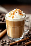 Tasse de café au lait avec crème fouettée et caramel, entourée de grains de café et cannelle.