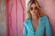 © imagemir - A stylish young woman stands against a vibrant pink wall, wearing sunglasses and a light blue jacket, exuding a confident and modern vibe.