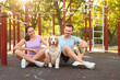 © Pixel-Shot - Young couple with Australian Shepherd dog sitting on sport ground