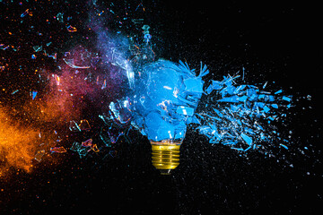 Fototapete - Broken blue light bulb exploding with colorful powder on a black background