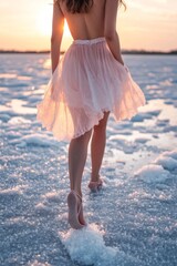 Leinwandbilder - A woman walks gracefully across a shimmering icy landscape, her soft pink dress catching the golden hues of sunset