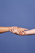 © Seventyfour - Close-up shot showing two hands holding each other, symbolizing unity, trust, and connection against a blue background