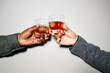 © Seventyfour - Two hands holding glasses of dark beverage clinking against plain light background, depicting casual celebration without visible facial expressions in minimalist setting