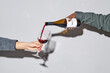 © Seventyfour - Hand seen pouring red wine from bottle into glass against plain gray wall, creating shadow on surface during action, showcasing simple, elegant moment