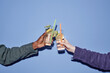 © Seventyfour - Close-up shot of two hands clinking glasses filled with summer cocktails, featuring lemon slices and straws against a blue backdrop, embodying celebration and enjoyment
