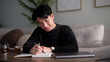 © wattana - Man writing in a notebook while enjoying tea in a cozy home setting.