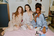 © AnnaStills - Portrait of smiling and relaxing friends in silk and cotton pajamas sitting on bed after manicure at home