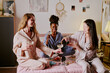 © AnnaStills - Wide shot of brunette woman in silk pajamas pouring polish glass of expensive champagne during sleepover