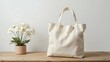 © RiadArt - Elegant beige tote bag on a wooden table with a potted white flower. Minimalist, eco-friendly fashion concept with soft natural lighting and neutral tones. Perfect for mockup and lifestyle themes.