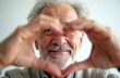 © Maryna - Happy senior man makes heart shape hand gesture, smiles at camera. Elderly grandparent shows romantic symbol of love and self-care. Retired pensioner, looking at you with love, gratitude, charity.