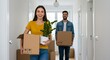 © rdkcho - Happy Young Couple Moving into New Home, Carrying Boxes and a Houseplant, Smiling and Excited for New Beginning