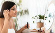 © Prostock-studio - Side view of young asian woman looking at mirror, applying mascara, home interior, copy space. Cheerful attractive lady in homewear sitting in bedroom, using mascara, getting ready before going out