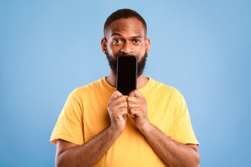 Poster - handsome african american man covering is mouth with blank cellphone with mockup for app or website 